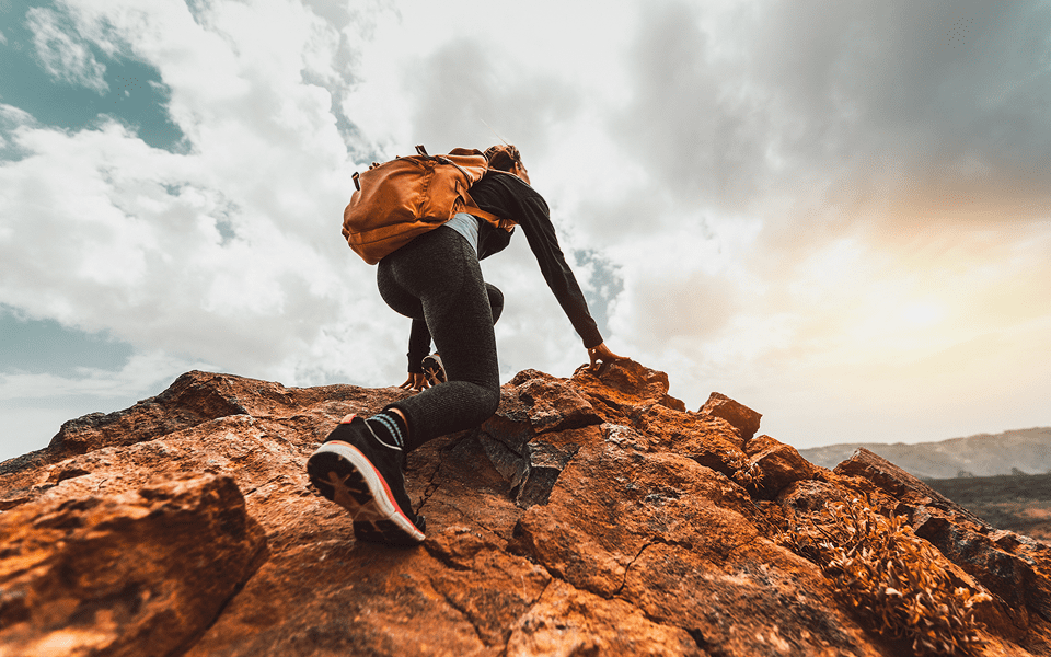 Person climbing rocky hill under cloudy sky.