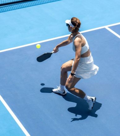 Woman playing tennis on a blue court, preparing to hit the ball.
